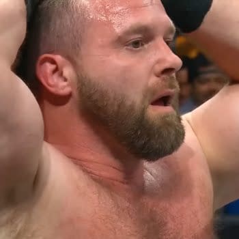 A close-up of a muscular man, Cash Wheeler of FTR, with a beard, showing an intense expression as he holds his head in a wrestling ring, during a moment of tension.