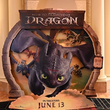 A promotional standee for 'How to Train Your Dragon' featuring a large, detailed depiction of the dragon Toothless with glowing green eyes, flying with characters on its back, and other dragons in the background. The standee includes the text 'IN THEATERS JUNE 13' at the bottom.