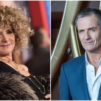 Amy Pascal, a woman with curly hair and wearing a black outfit, smiles on the left, while David Heyman, a man in a blue suit with short hair, poses on the right. This image highlights the producers of the next James Bond film.