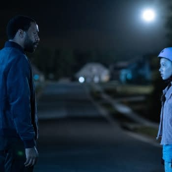 A still from 'The Life of Chuck' shows a man and a girl in a dimly lit neighborhood at night. The man stands in profile wearing a blue jacket, while the girl, wearing a blue helmet, looks towards him with a concerned expression.