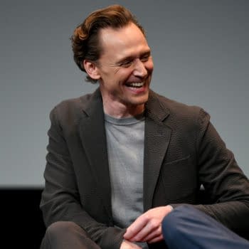Tom Hiddleston, wearing a dark blazer and gray shirt, smiles while speaking onstage at the LOKI S2 Official Emmy FYC Event in Beverly Hills, California.