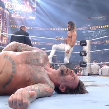 CM Punk is laid out in the wrestling ring, visibly defeated, while Seth Rollins stands triumphantly in the background, and Paul Heyman exits the scene. Bright lights illuminate the WrestleMania 41 event atmosphere.