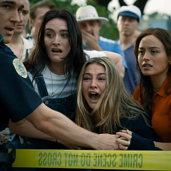 A tense scene featuring a police officer holding back a crowd, while three women display fear and distress, particularly one who is crying out. Yellow crime scene tape is visible in the foreground, contributing to the dramatic atmosphere.