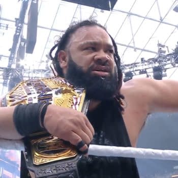 Jacob Fatu, wearing a black tank top, celebrates with the United States Championship belt, showcasing a proud and intense expression. The background features bright arena lights and a large banner.