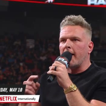 Pat McAfee enthusiastically delivers a promo from atop the commentary desk during WWE Raw, with a lively crowd visible in the background.