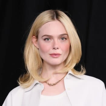 A portrait of a woman with long blonde hair, wearing a white shirt and a necklace, against a dark background, possibly related to Elle Fanning and her potential casting in a project titled 'Sunrise on the Reaping'.