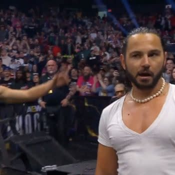Two members of the Young Bucks appear onstage during an AEW event, with a cheering crowd behind them, as one gestures dramatically. The atmosphere is charged with excitement.
