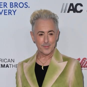 Alan Cumming poses in a stylish green and beige jacket, smiling in front of a backdrop with logos for Warner Bros. Discovery and American Cinematheque, relevant to his discussion on Nightcrawler's return in Avengers: Doomsday.