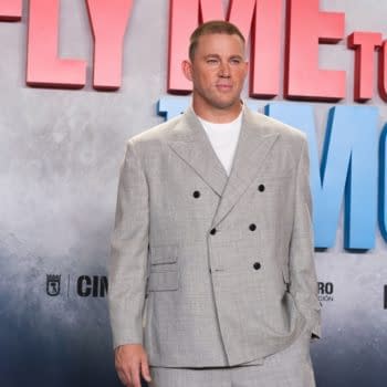 Channing Tatum stands confidently at a photocall for the movie "Fly Me to the Moon," wearing a stylish gray suit. The backdrop features the title of the film in bold, colorful lettering.