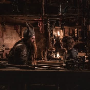 A scene from 'How To Train Your Dragon' featuring a bearded character in armor speaking to a young boy in a dimly lit workshop filled with various tools and decorations.