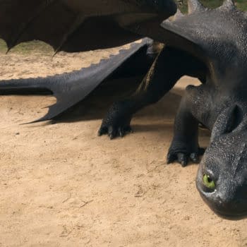 A stylized dragon with glossy black scales and large green eyes is crouched on a sandy surface, its wings partially extended. The scene appears to be set in a natural outdoor environment.