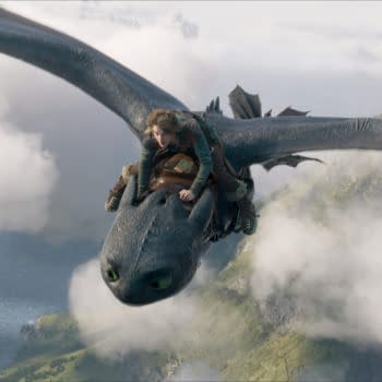 A character from 'How To Train Your Dragon' is riding on the back of a large, black dragon soaring above clouds and a coastline, capturing a sense of adventure and freedom.