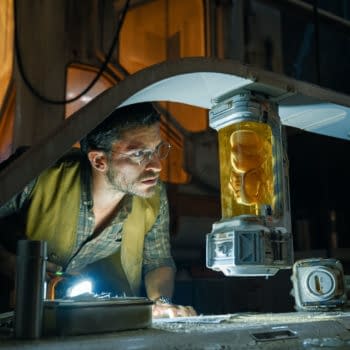 A scene from 'Jurassic World Rebirth' featuring Jonathan Bailey as Dr. Henry Loomis, intensely examining a yellow container holding a dinosaur embryo under a dim light, in a lab-like environment.