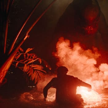A tense scene from 'Jurassic World Rebirth,' featuring a silhouetted figure in water, illuminated by a glowing object, with a menacing dinosaur emerging in the background, surrounded by dark foliage and smoke.