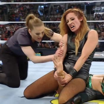 Becky Lynch applies pressure on Lyra Valkyrie's arm while an official intervenes during a WWE match. The background features a cheering crowd and wrestling ring elements.