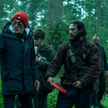 A group of four people in a forest, with one wearing a red beanie and gesturing, while another holds an arrow and bow. The scene conveys a sense of urgency and focus, suitable for a narrative about survival or adventure.