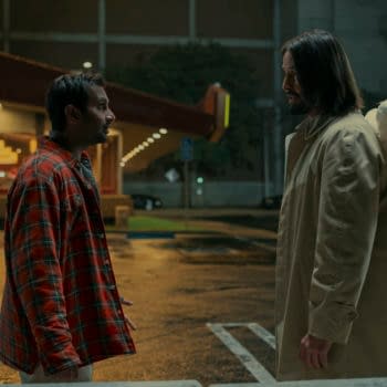 A scene from the film "Good Fortune" featuring Aziz Ansari as Arj and Keanu Reeves as Gabriel, who appears with angel wings. The setting is a dimly lit parking lot with a Denny's restaurant in the background.
