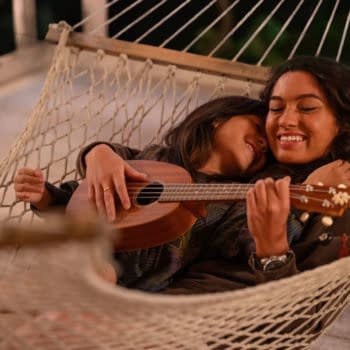 Two young women relax together in a hammock, with one playing a ukulele. The scene captures a warm and intimate moment, highlighting the bond between Lilo and her older sister Nani from Disney's live-action adaptation of 'Lilo & Stitch.'