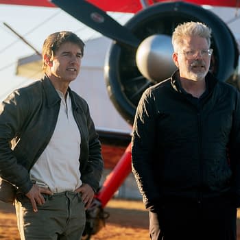 Tom Cruise and Christopher McQuarrie stand on the set of 'Mission: Impossible - The Final Reckoning' in front of a biplane during sunset, with a warm light illuminating the scene.