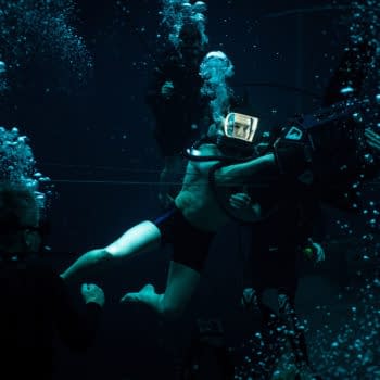 A scene from 'Mission: Impossible - The Final Reckoning' shows a diver in an underwater setting, wearing a helmet and interacting with filming equipment, surrounded by bubbles and other divers.