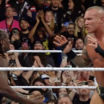 R-Truth intervenes as Randy Orton prepares to deliver an RKO to John Cena during a WWE Backlash event, surrounded by an excited crowd.