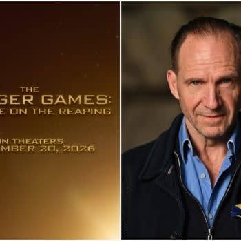 A promotional image from 'The Hunger Games: Sunrise on the Reaping,' featuring actor Ralph Fiennes with a serious expression, wearing a blue shirt and a black coat, and a ribbon pinned to his lapel. The background is softly blurred, focusing on Fiennes as the text for the movie is displayed prominently in gold.