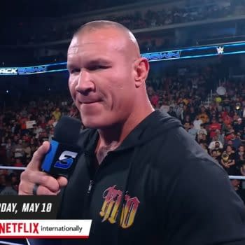 Randy Orton delivers a promo on WWE SmackDown, speaking into a microphone in front of a cheering crowd. He wears a black hoodie with a colorful design, emphasizing an intense moment in the ring.