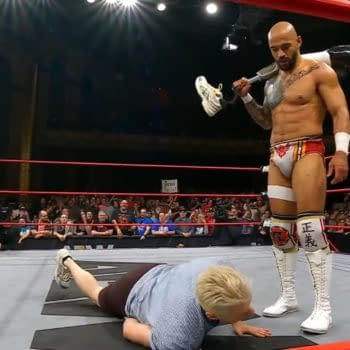 A muscular wrestler, Ricochet, stands triumphantly over Zach Gowen, who is on the mat. Ricochet holds Gowen's own prosthetic leg as a symbolic act during an AEW Collision event.