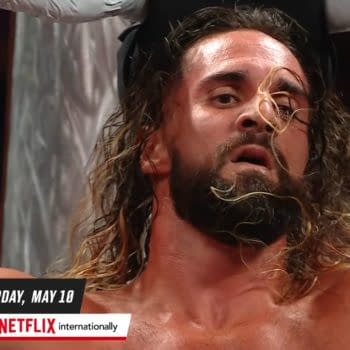 Seth Rollins, a professional wrestler, appears sweaty and intense during a match on WWE Raw, with his long hair partially covering his face and a background of wrestling ring ropes and fans.