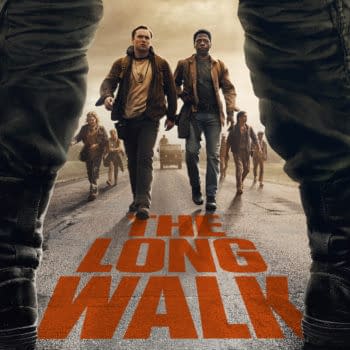 A movie poster for 'The Long Walk' featuring two young male characters in the foreground, walking on a deserted road with a group of people behind them. The title appears prominently in bold orange text at the bottom, and military vehicles are visible in the background.
