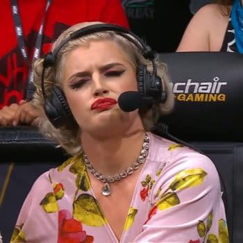 A commentator with blonde hair and bold makeup, dressed in a floral blouse, looks skeptically while speaking into a microphone, headset on. The background shows a diverse audience at an AEW event, highlighting a mix of expressions from fans.