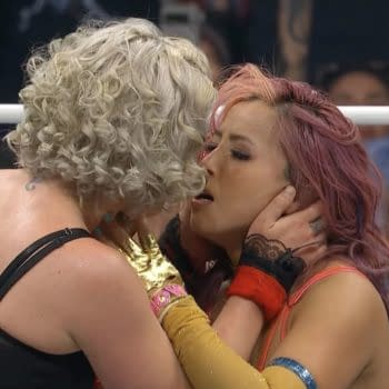 Toni Storm and Mina Shirakawa share a respectful kiss in the wrestling ring, showcasing a moment of sportsmanship after their match. Both wrestlers have distinct hairstyles and colorful wrestling attire.