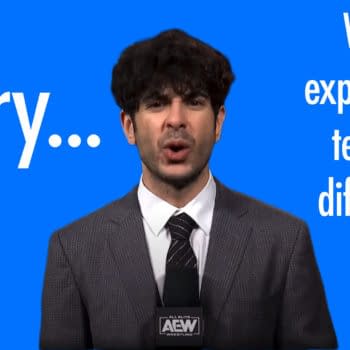 A man in a gray suit with a microphone in front of a bright blue background, AEW owner Tony Khan, apologizes and announces technical difficulties. The large text beside him says 'Sorry...' and 'We are experiencing technical difficulties.'
