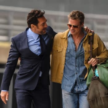 Two men walk closely together, one wearing a suit and tie and the other in a casual outfit with sunglasses, both appearing friendly in a setting likely related to Formula 1.
