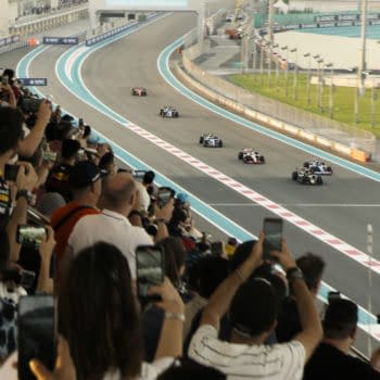 F1: A crowd of enthusiastic Formula 1 fans captures the excitement of a race on their smartphones, as several cars compete on a winding racetrack. The vibrant atmosphere is heightened by the spectators' cheers and the colorful team apparel.