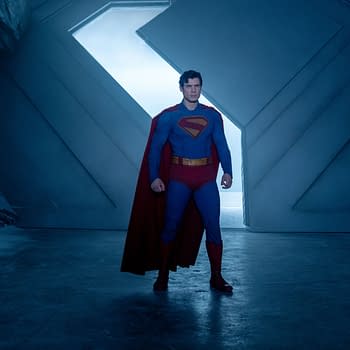 Superman stands confidently in a futuristic ice cave, wearing his iconic blue suit with a red cape. Crystalline structures are visible in the background against a blue-lit atmosphere.