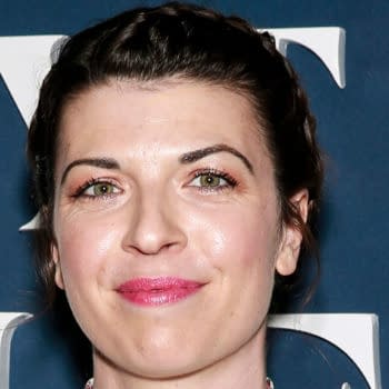 Megan Ganz smiles at the premiere of Apple TV+'s 'Mythic Quest: Raven's Banquet' in Los Angeles, showcasing her styled hair and vibrant makeup against a blue backdrop.