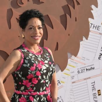 Liza Colón-Zayas poses confidently at the premiere of 'The Bear', wearing a floral-patterned dress against a backdrop of film-related materials and an artistic representation of a bear.