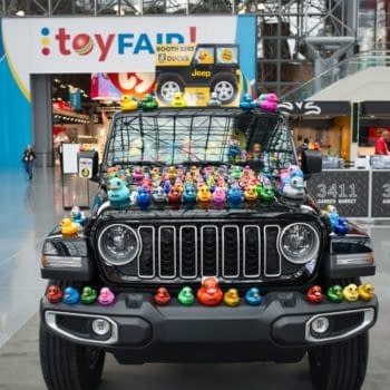 A black Jeep Wrangler decorated with colorful rubber ducks displayed at a toy fair. The background features a vibrant toy fair banner.