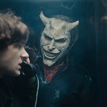A tense scene from Black Phone 2 features a young boy speaking on a telephone while a sinister figure wearing a devil-like mask looms behind him. This illustration captures the suspenseful atmosphere of the horror film.