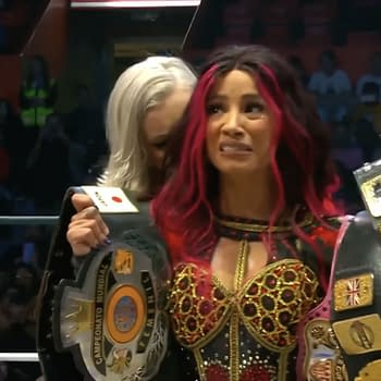 Mercedes Moné celebrates with her championship belts after winning the CMLL Women’s Championship at AEW Grand Slam Mexico, her expression a mix of joy and shock as she becomes aware of the presence of Timeless Toni Storm directly behind her.