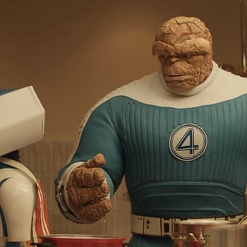 A scene from 20th Century Studios' 'The Fantastic Four: First Steps' featuring H.E.R.B.I.E, a robotic character, next to Ebon Moss-Bachrach as Ben Grimm/The Thing, who has a rocky appearance and is wearing a blue costume with a large number 4. They are in a kitchen setting.