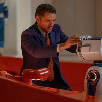 Pedro Pascal portrays Reed Richards/Mister Fantastic in a scene from 'The Fantastic Four: First Steps,' interacting with a futuristic robot in a brightly colored laboratory setting.