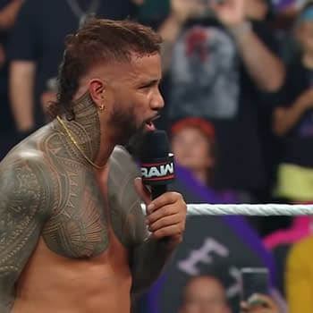 Jey Uso, a professional wrestler, delivers a passionate promo from the ring after losing the title to Gunther, with a crowd of fans in the background. His muscular build and intricate tattoos are prominently displayed as he holds a microphone.