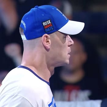 John Cena, wearing a blue and white cap with the words 'Rise Above Hate,' appears in profile during a WWE SmackDown event, showcasing his determined expression and iconic look.
