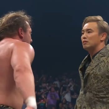 Kenny Omega and Kazuchika Okada face each other intensely during AEW Fyter Fest, capturing a moment of confrontation between two wrestling stars. Omega, with his long hair and muscular physique, faces Okada, who is dressed in an ornate jacket, emphasizing the tension of their rivalry.