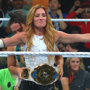 Lyra Valkyria places the championship belt on Becky Lynch, who stands with her arms outstretched in celebration after winning the title at WWE Money in the Bank. Fans are visible in the background, capturing the moment.