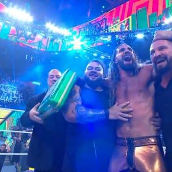 Seth Rollins celebrates winning the Men's Money in the Bank match, surrounded by teammates, with a green briefcase in hand and an arena full of lights in the background.