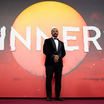 Director Ryan Coogler stands at the European premiere of "Sinners," against a bold backdrop featuring the film's title and a large sun graphic.
