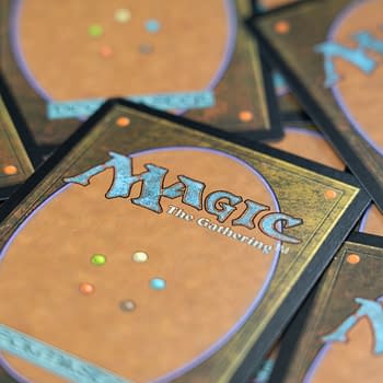 Colorful backs of Magic: The Gathering trading cards are stacked together, featuring an ornate design with a prominent logo and various colored dots, emphasizing the fantasy and gaming theme.